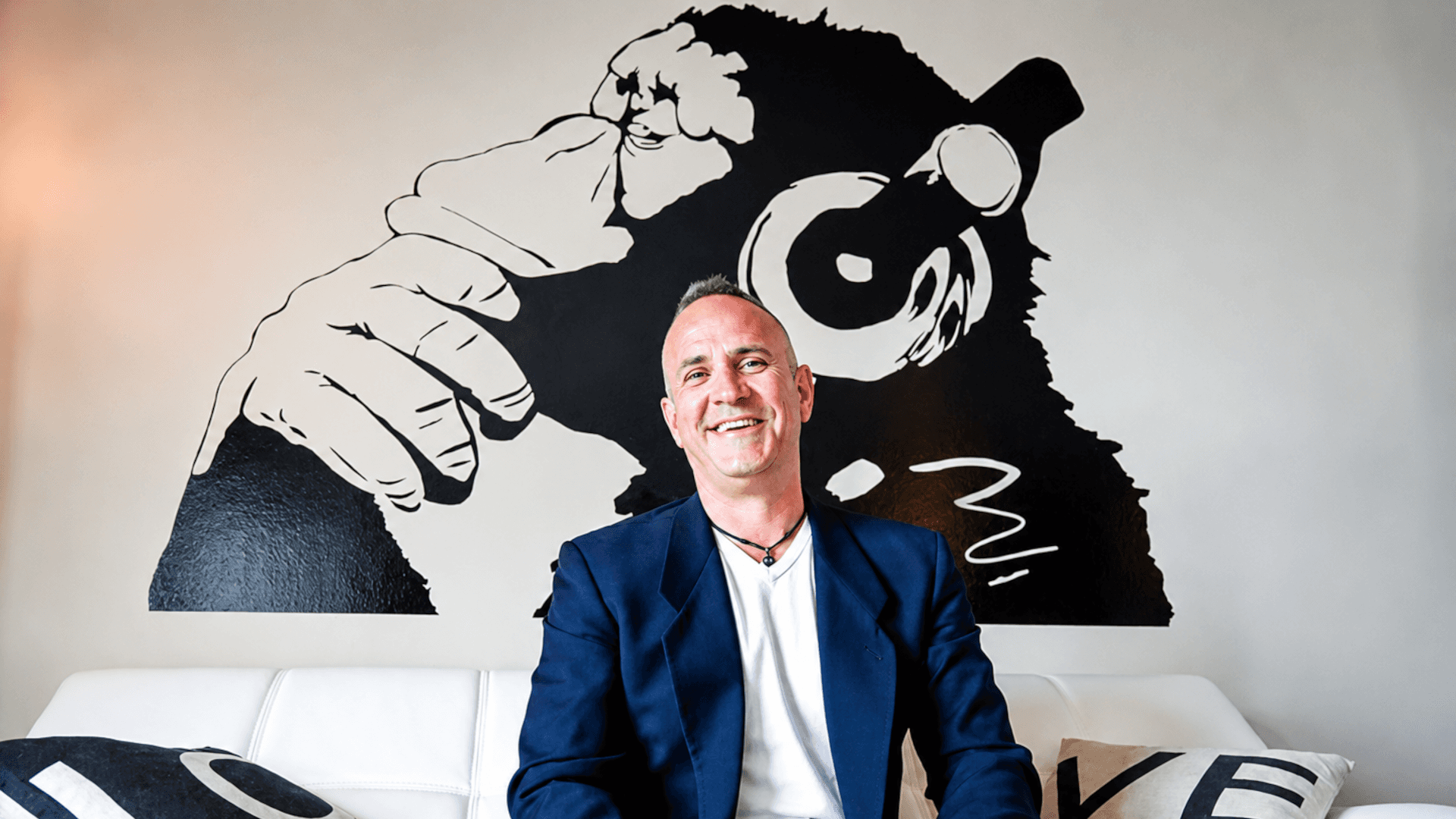 David Brown sitting on a white couch with a mural of a stylized monkey wearing headphones